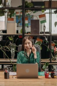 Smiling Asian woman in headset offering customer support services in an office setting.